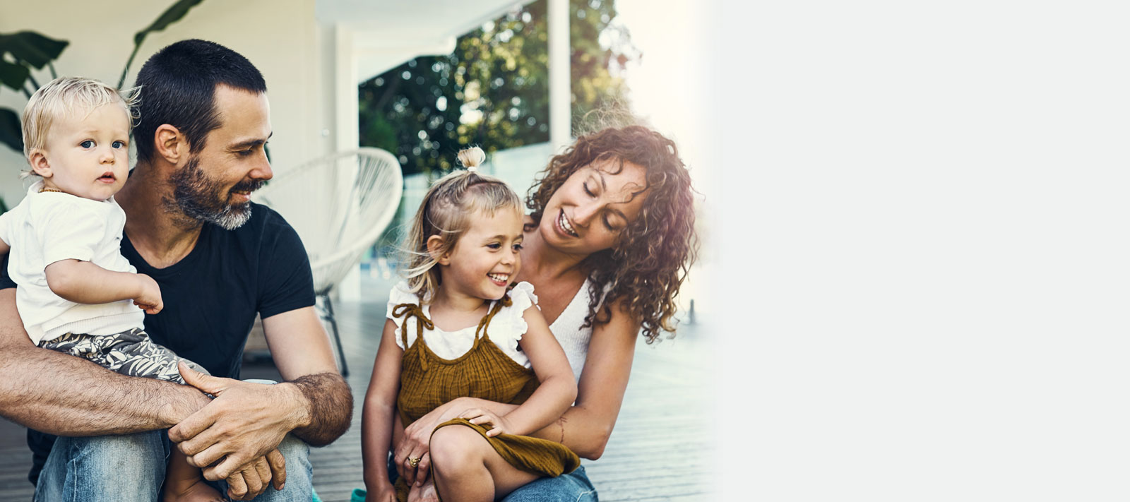 Mom, dad and two young child smiling while sitting on the front porch