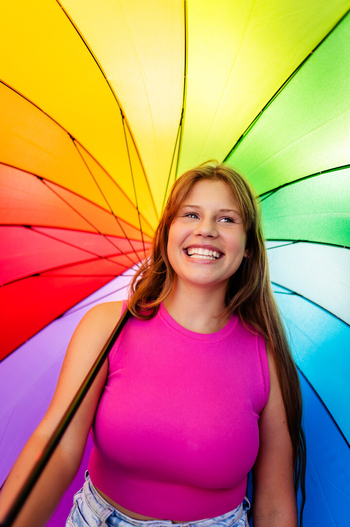 Happy beautiful pretty smiling young teen girl wearing bright pink top with colorful rainbow umbrella