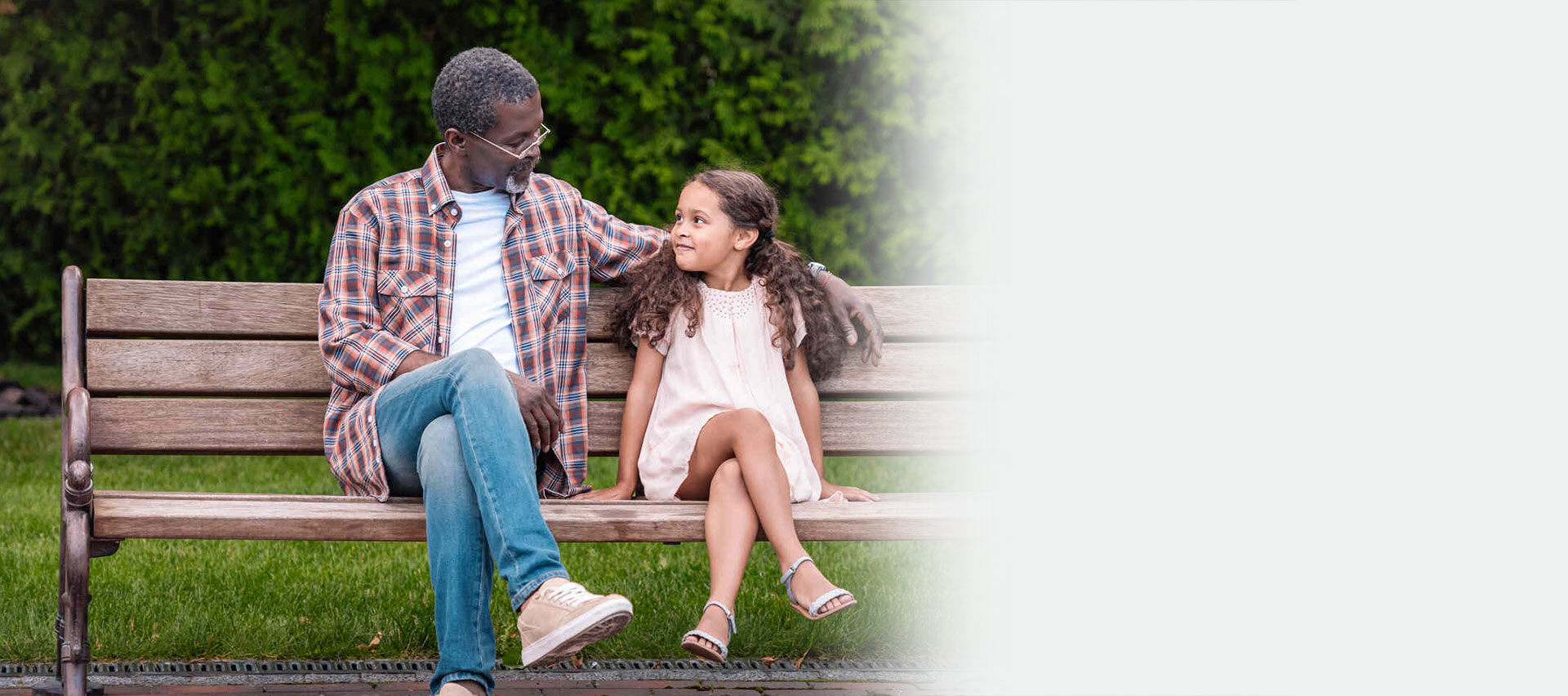 adorable african american girl and her grandfather sitting on bench in park